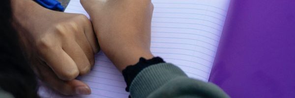 Close up of the hands and arms of two people writing in notebooks