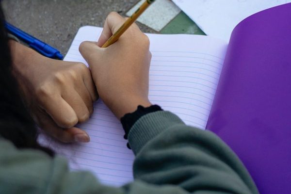 Close up of the hands and arms of two people writing in notebooks